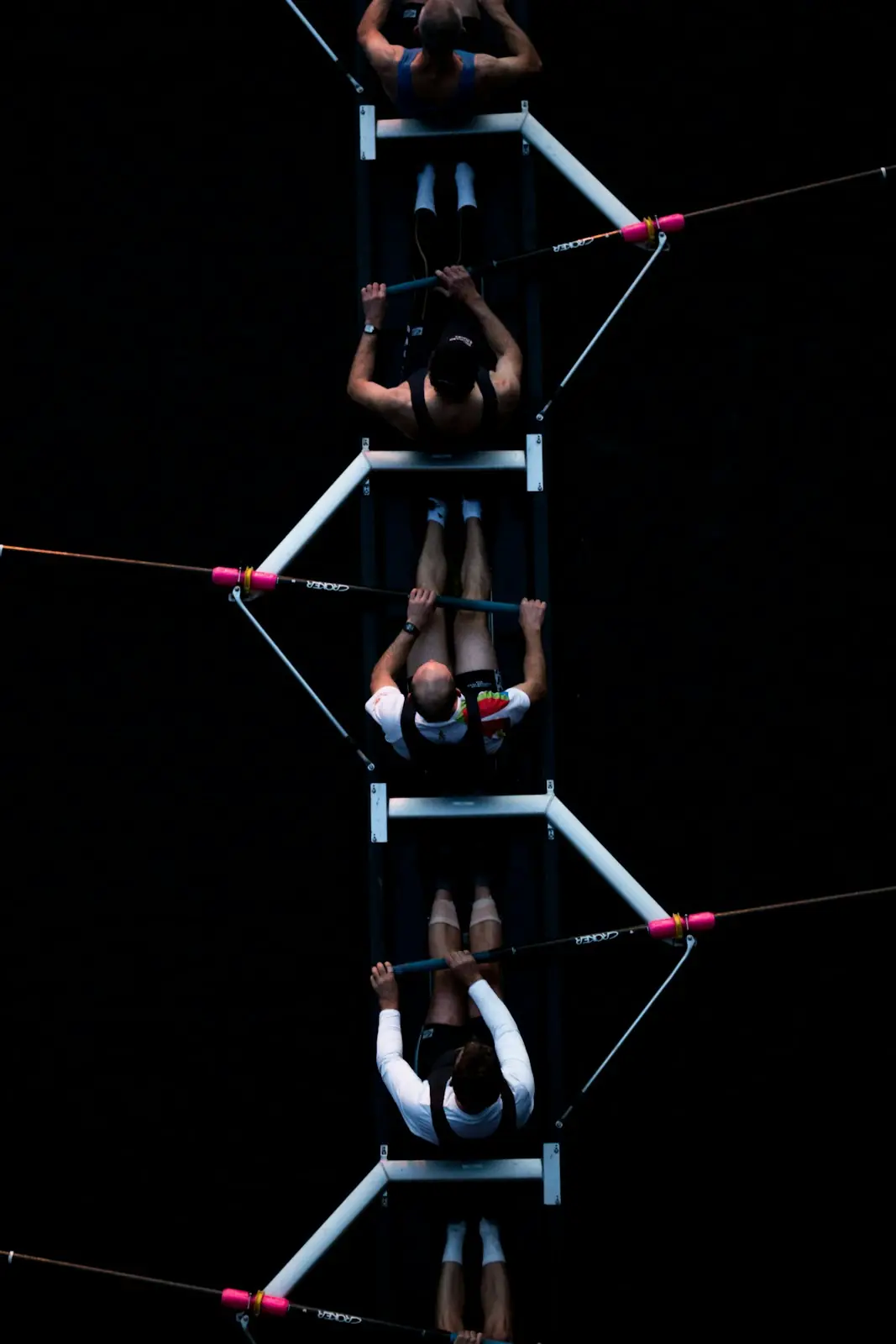 An overhead view of rowers in a narrow shell on black water, oars squared at the catch