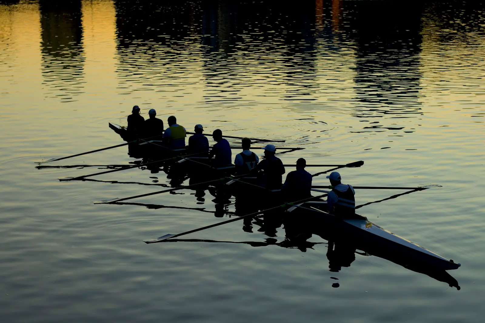 A rowing eight in silhouette on a calm river at sunset, golden light on the water