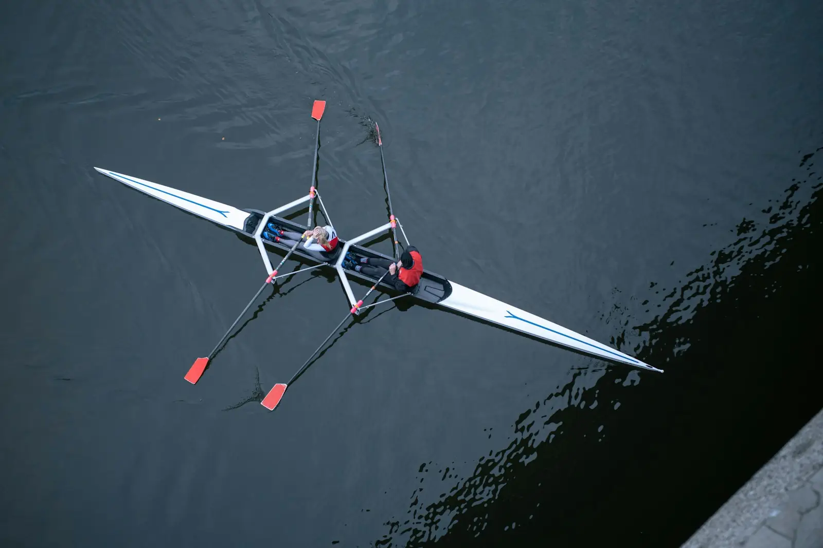 A single scull from above on dark water, the oars spread wide like wings
