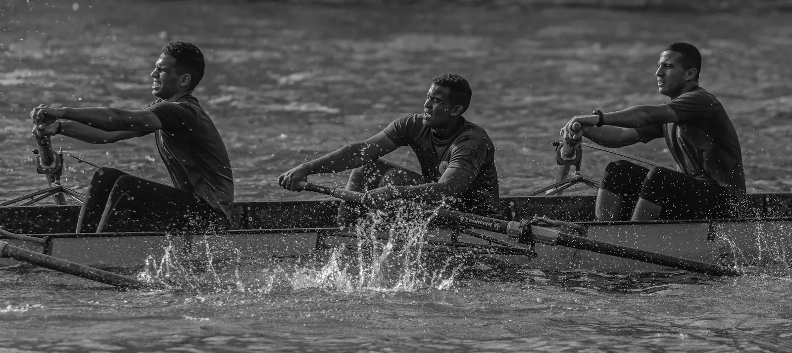 In black and white, rowers driving hard through spray at the catch