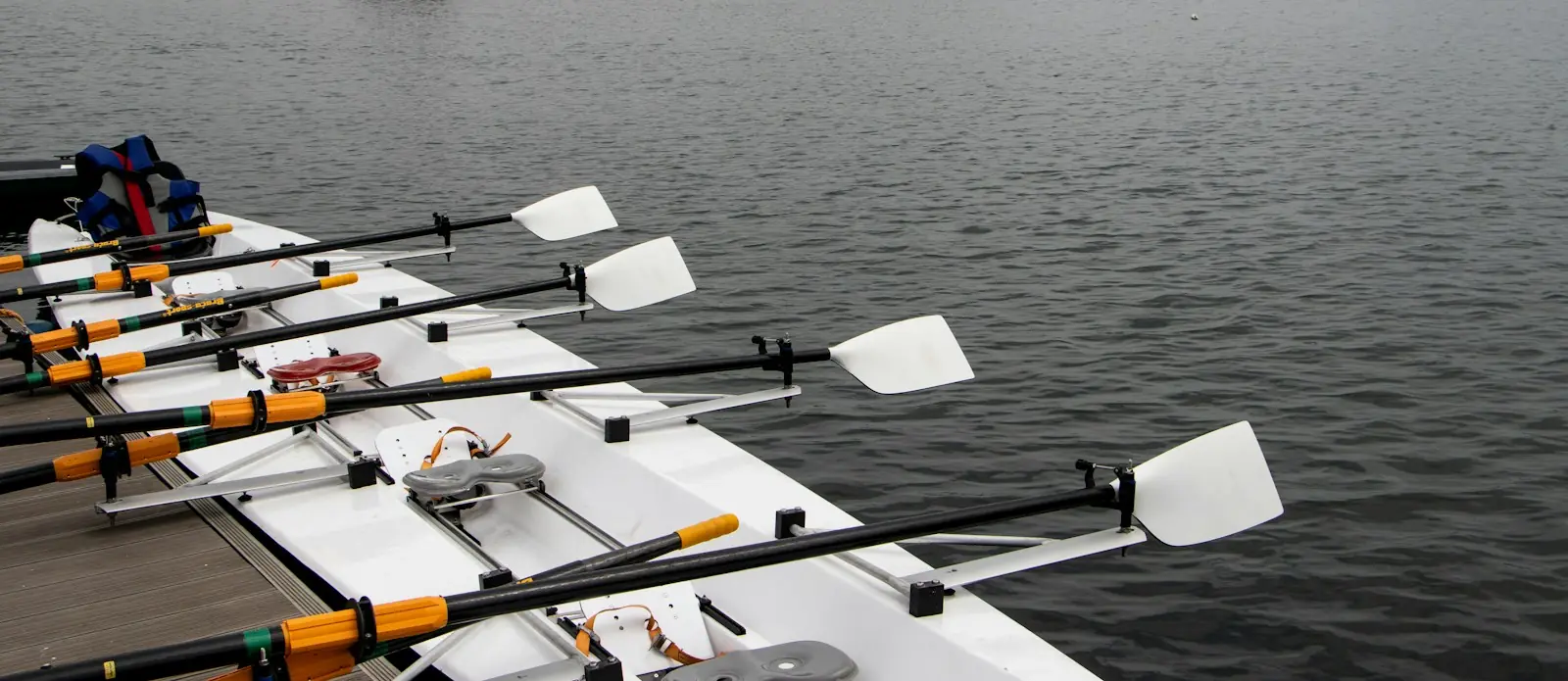 White oar blades resting on a line of boats moored at the bank, grey water beyond