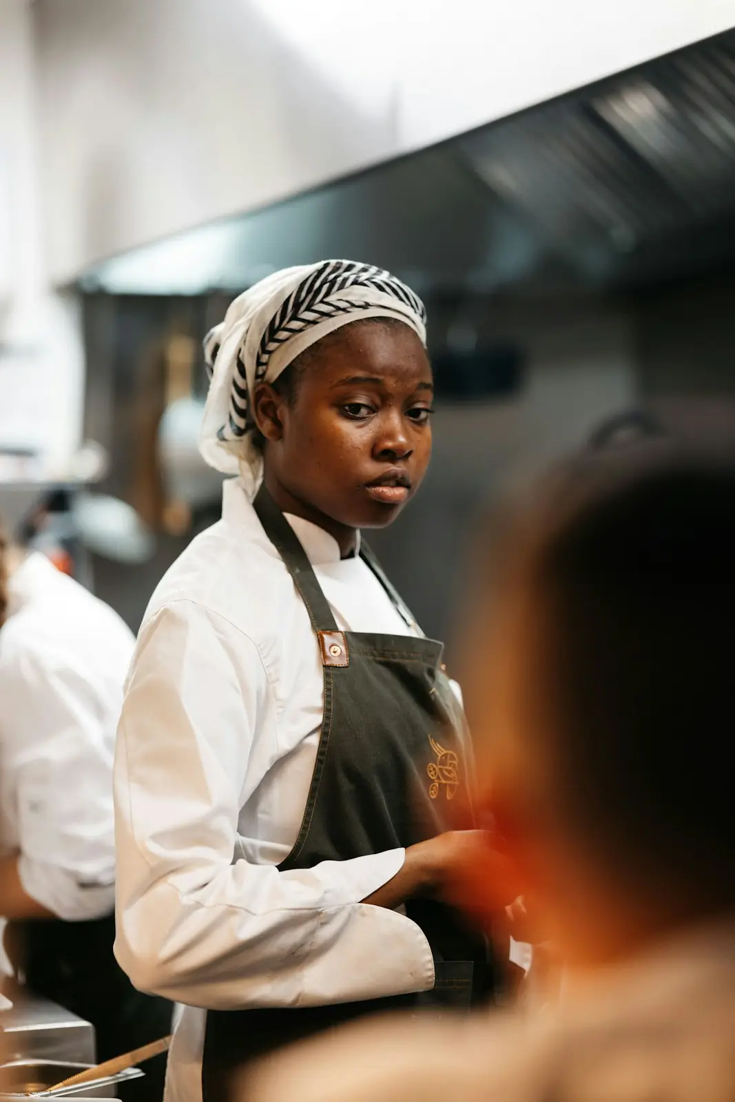Portrait of Amara Diallo in chef's whites and a headwrap, a dark apron tied at the waist