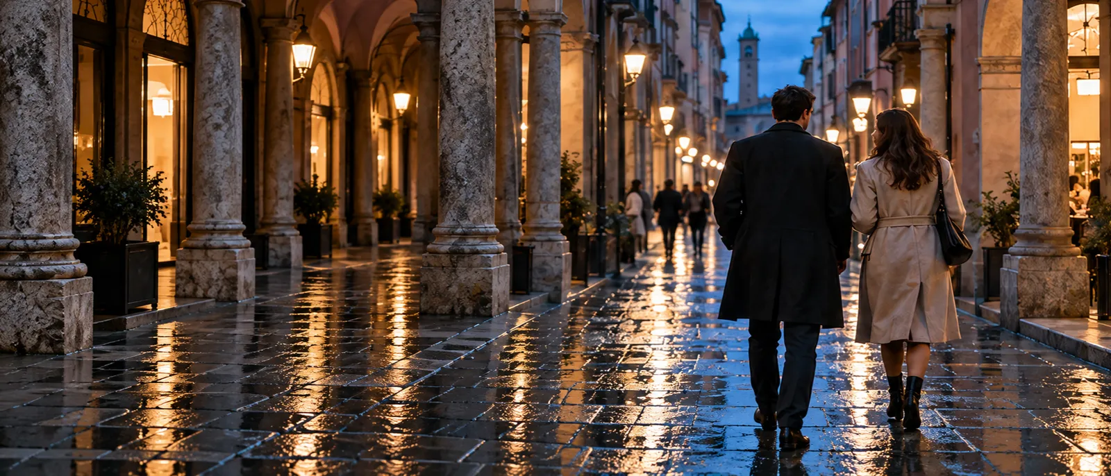 A couple walking away down a wet street under the porticoes at blue hour, shop windows glowing and a tower ahead