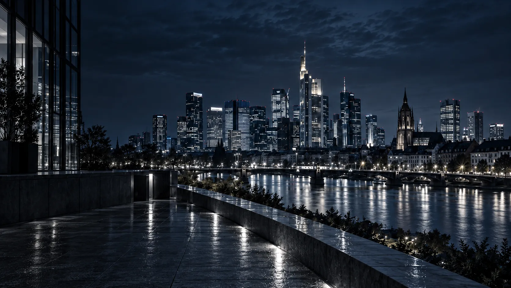 Eine nasse Steinterrasse bei Nacht neben einer Glasfassade, dahinter die beleuchtete Frankfurter Skyline über dem Main