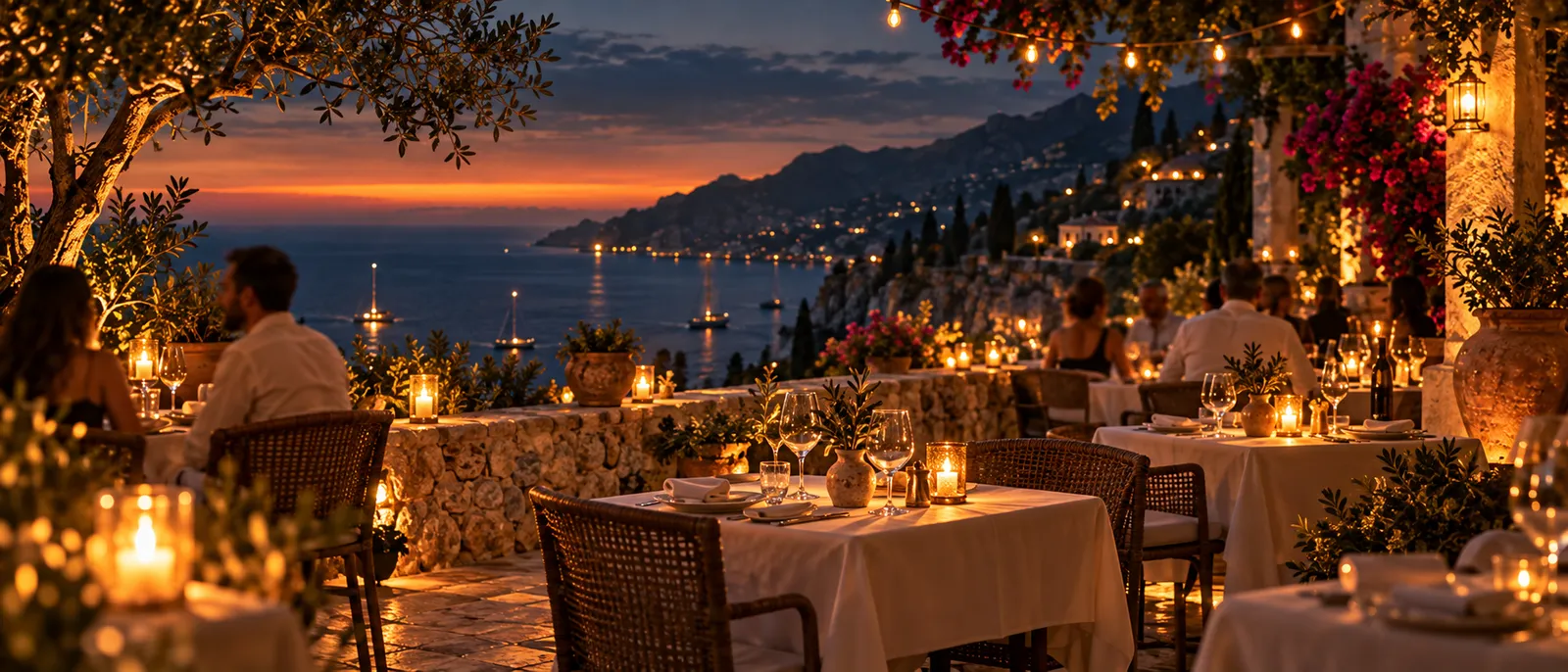 Candlelit tables along a stone terrace above the bay at dusk, guests dining under string lights