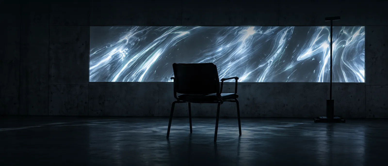 An empty chair facing a wide projection of liquid light in a dark room