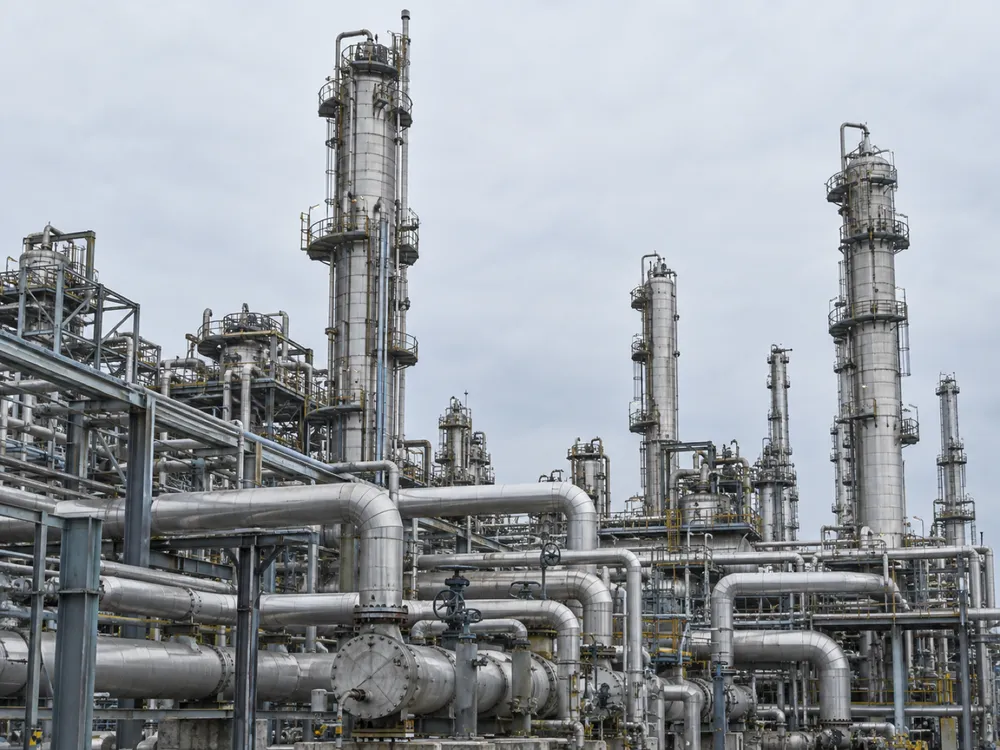 Industrial pipework and distillation towers under a pale sky