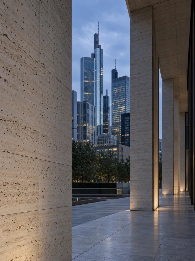 A travertine wall and steel-and-glass towers in Frankfurt at dusk