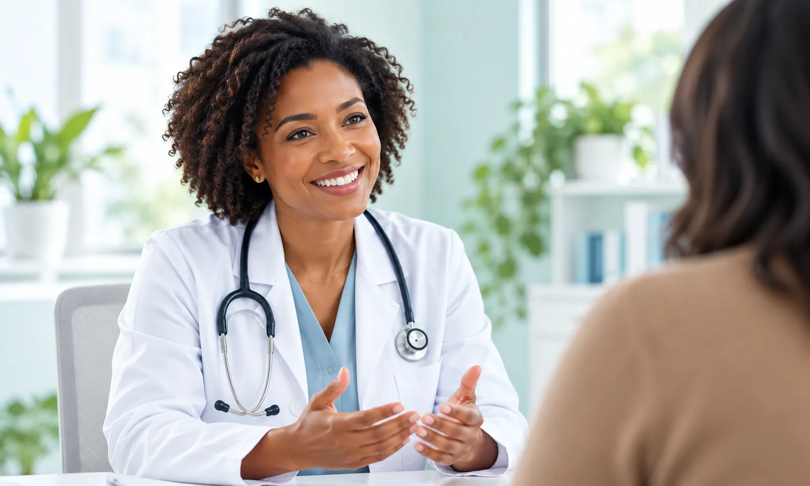 A smiling doctor with curly hair, in a white coat with a stethoscope, talking with a patient seen from behind