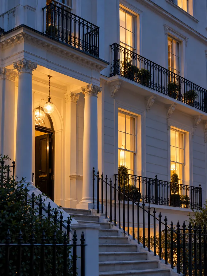 A white stucco terrace house with a columned porch and a lit fanlight above stone steps