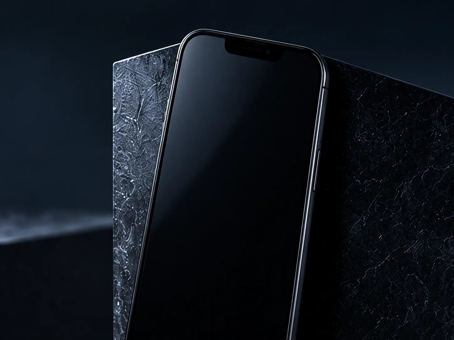 A black smartphone with its screen off leaning against a dark stone slab