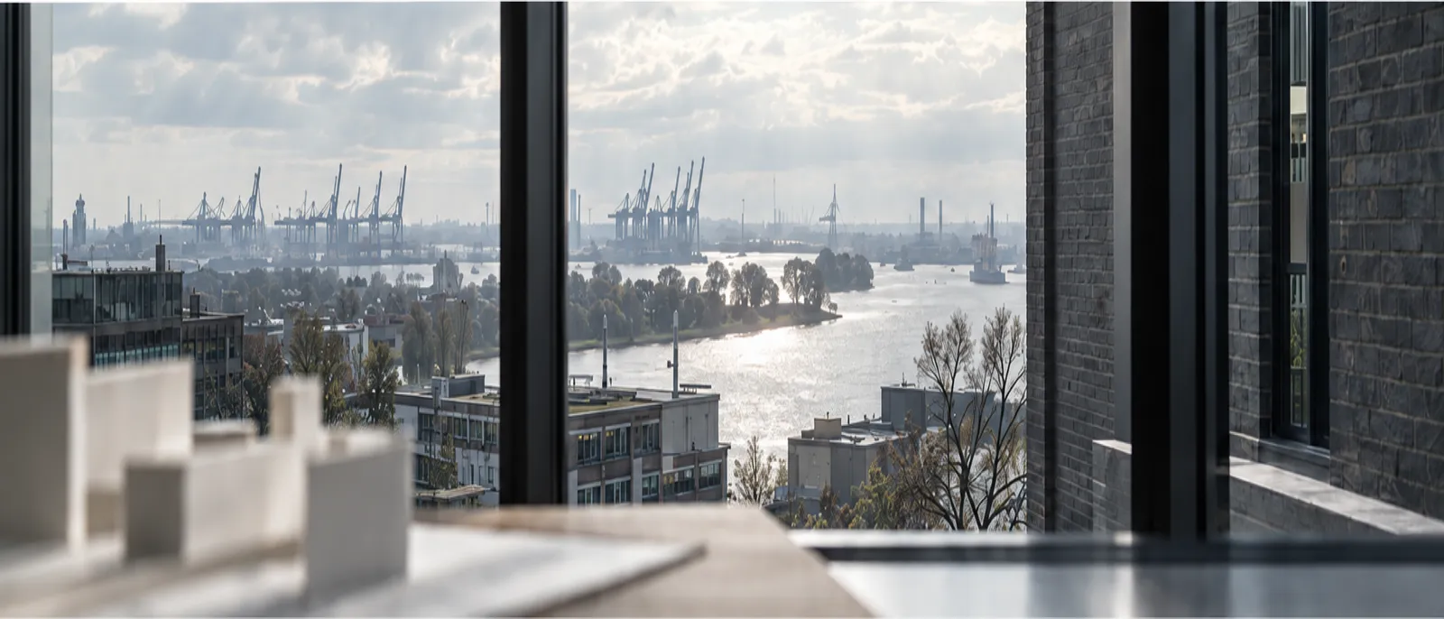 Blick aus dem Studiofenster über dunkle Klinkerdächer zur Elbe, vorn unscharf ein weißes Modell