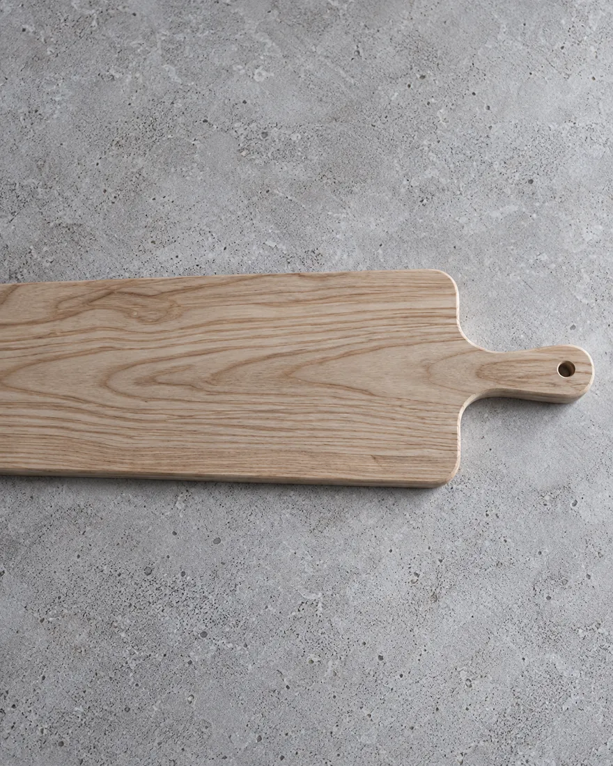 A pale ash serving board with a handle on a pale concrete surface