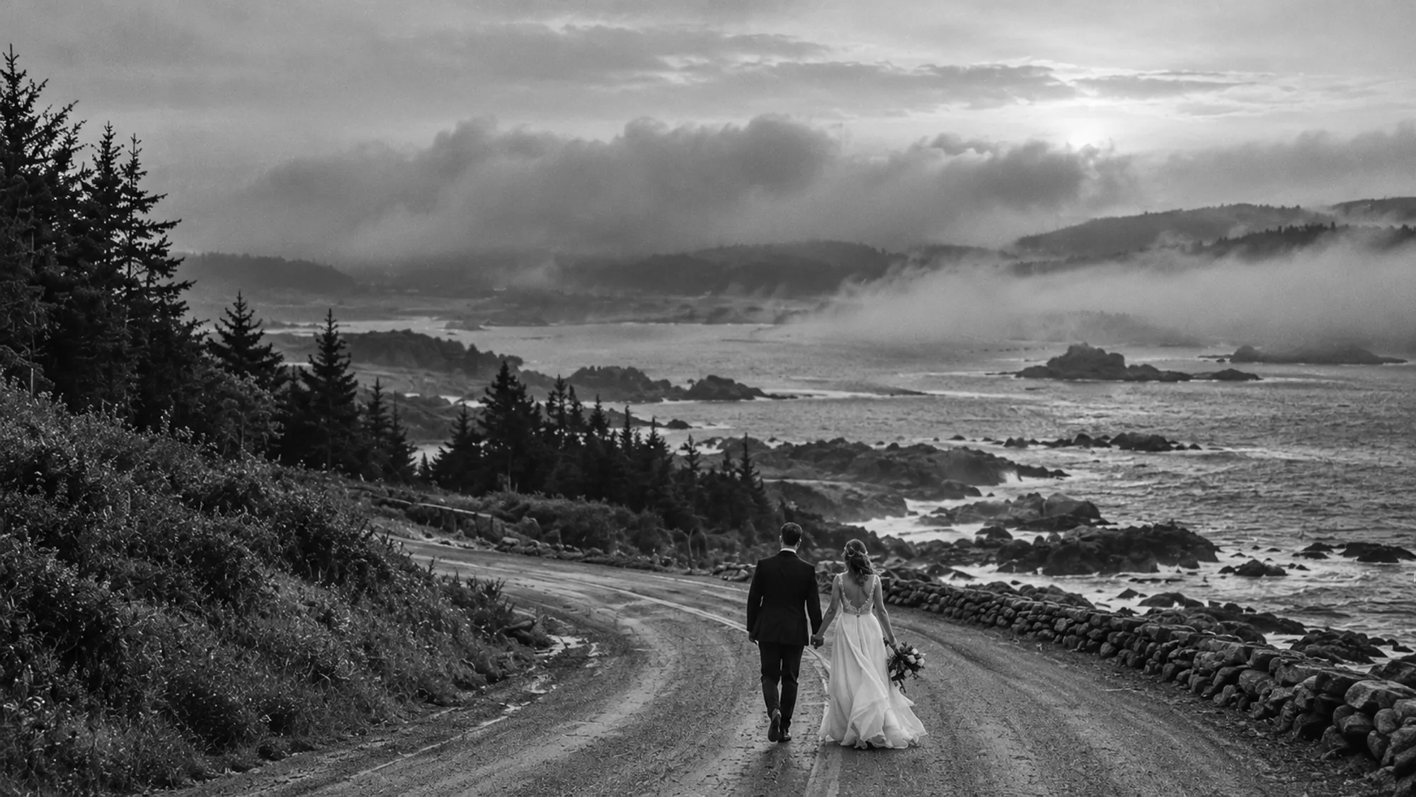 A couple walking hand in hand down a winding coastal road as sea fog rolls in