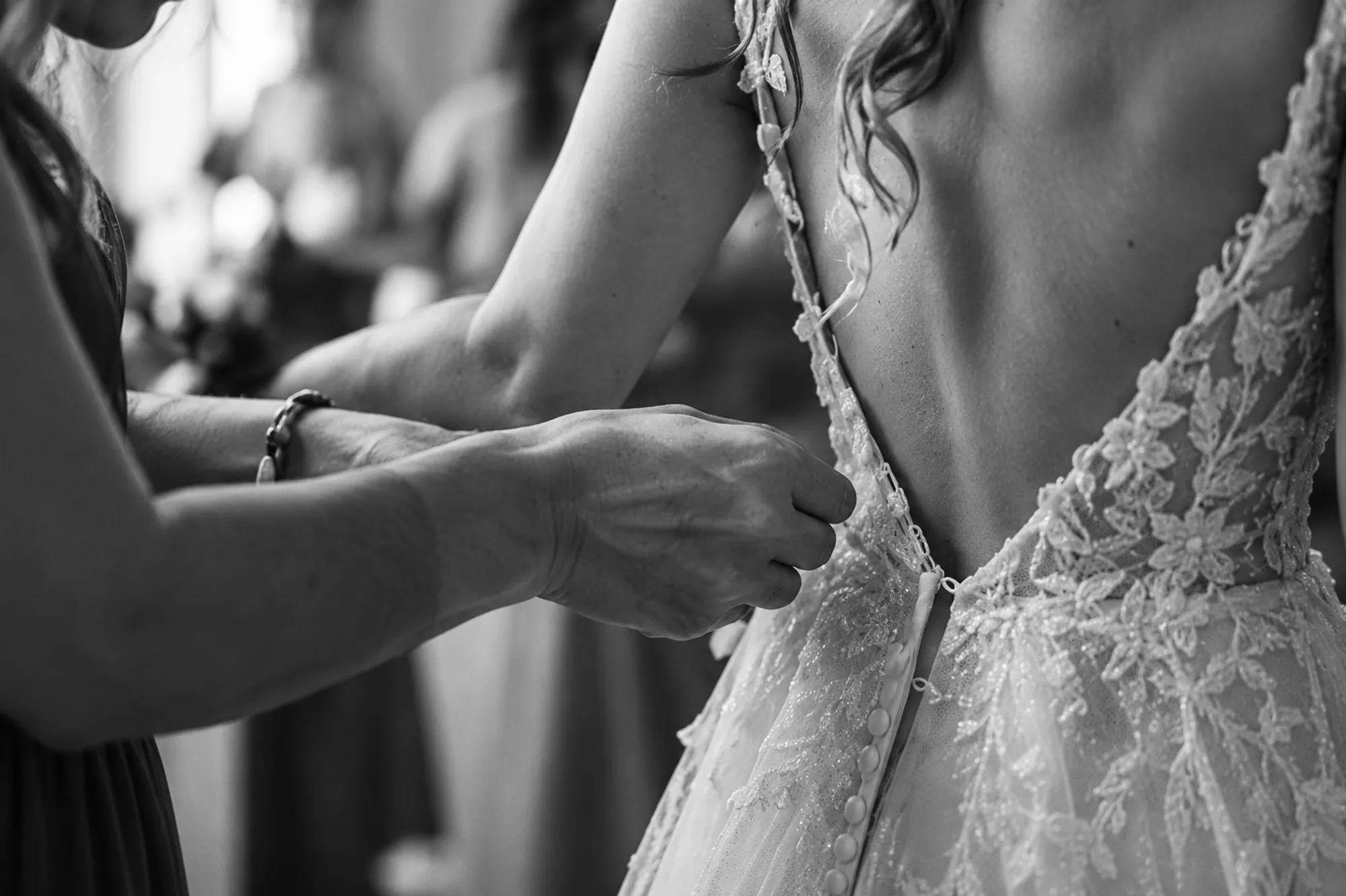 Hands fastening the buttons down the open back of a lace wedding dress