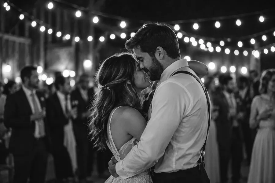 Bride and groom slow dancing close under strings of bulb lights at night