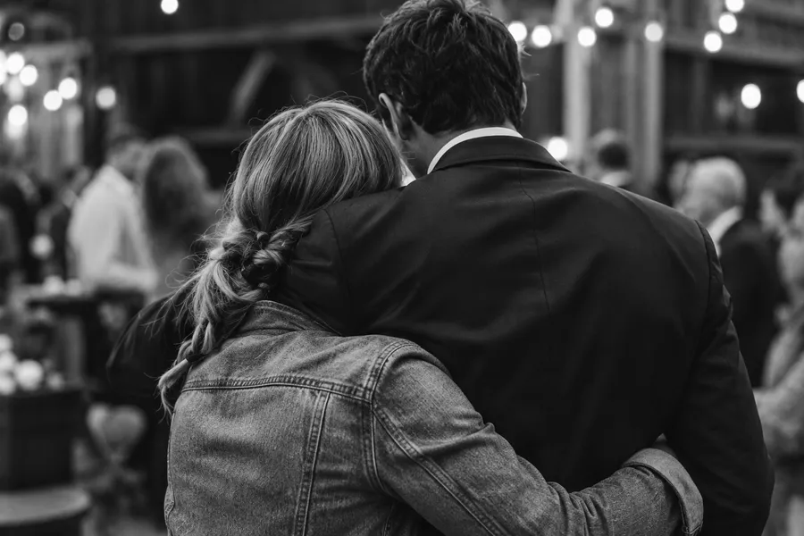 Two guests embracing, seen from behind: a woman with a long braid and a man in a suit