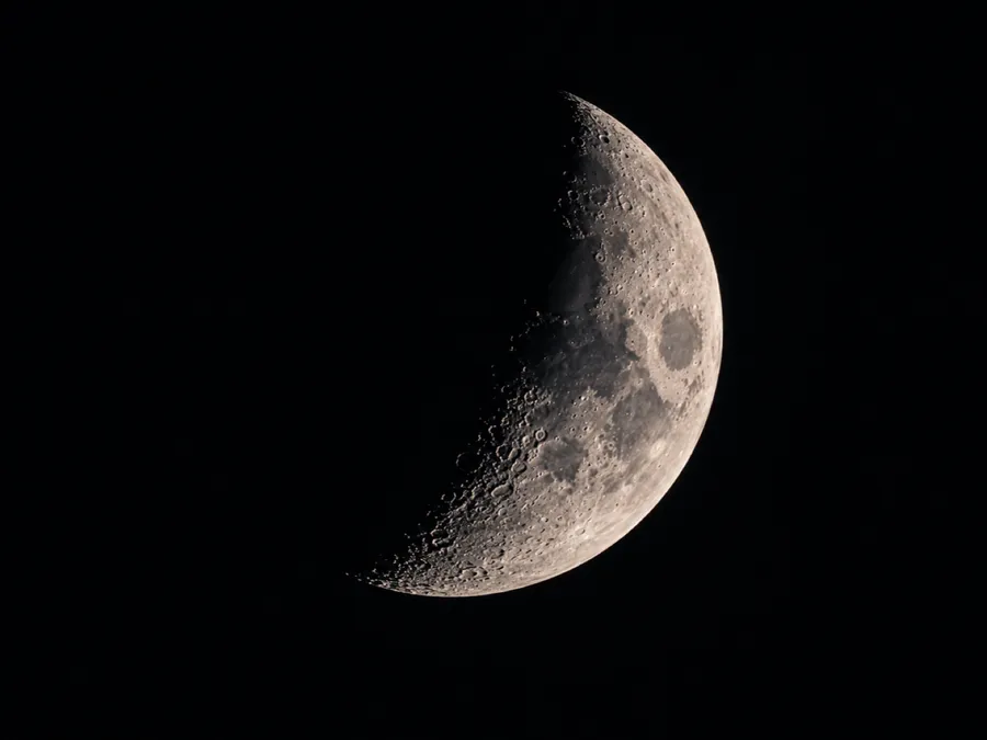 A crescent moon with sharp craters along its terminator