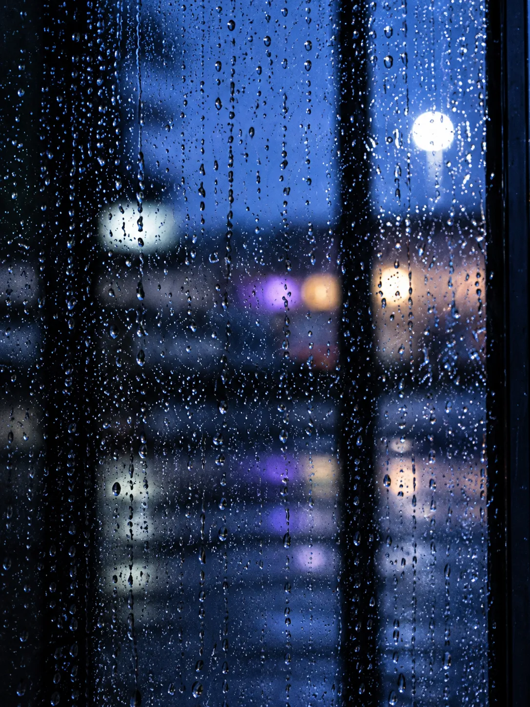 Rain on the glass of a workshop door at blue hour, street lights blurred beyond