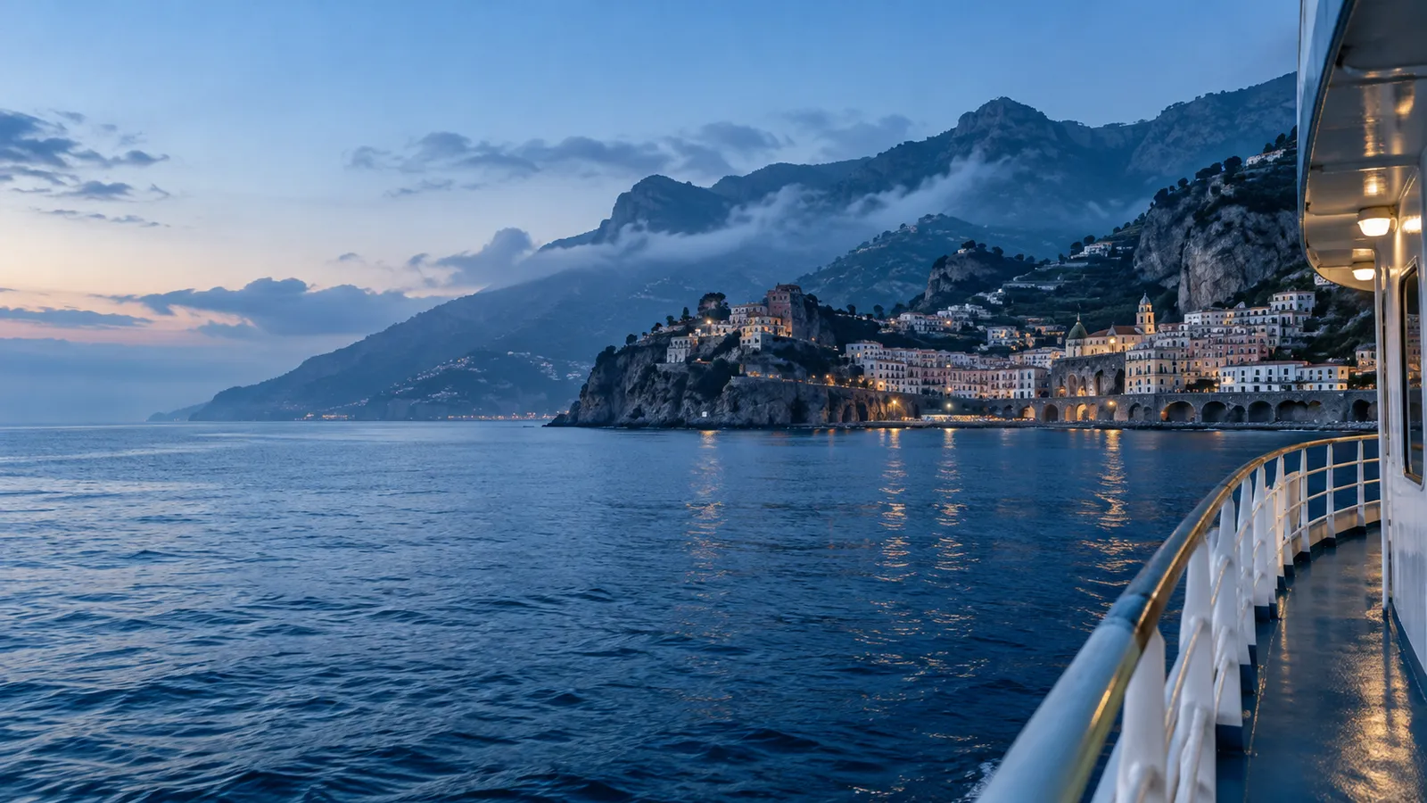From a ferry's deck at dawn, a hillside Italian town on a rocky headland across deep cobalt water, misty mountains behind