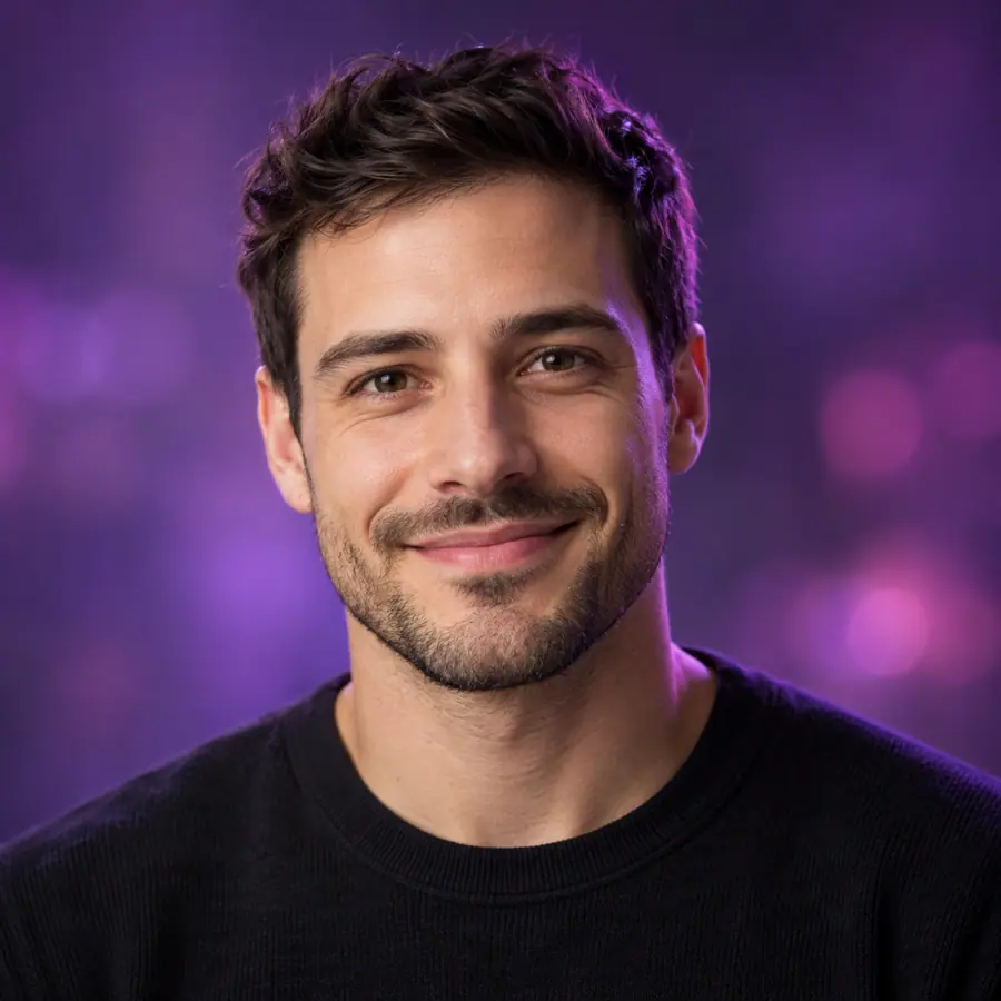 Portrait of Jason, smiling, with short dark hair and stubble, in a black jumper against a violet backdrop