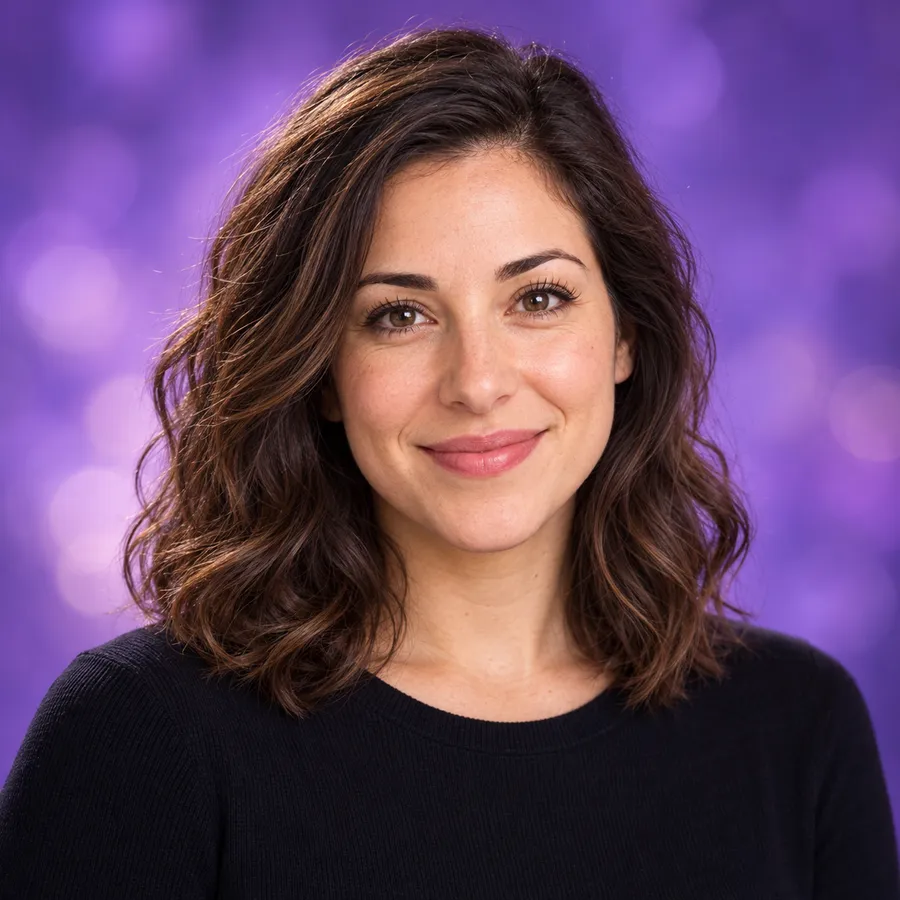 Portrait of Sarah, smiling, with shoulder-length wavy brown hair, in a black top against a violet backdrop